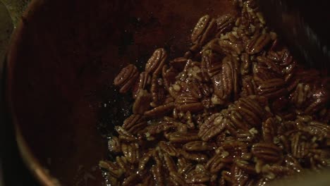 close up slow motion shot of roasted caramelised pecan nuts being stirred with a big wooden paddle