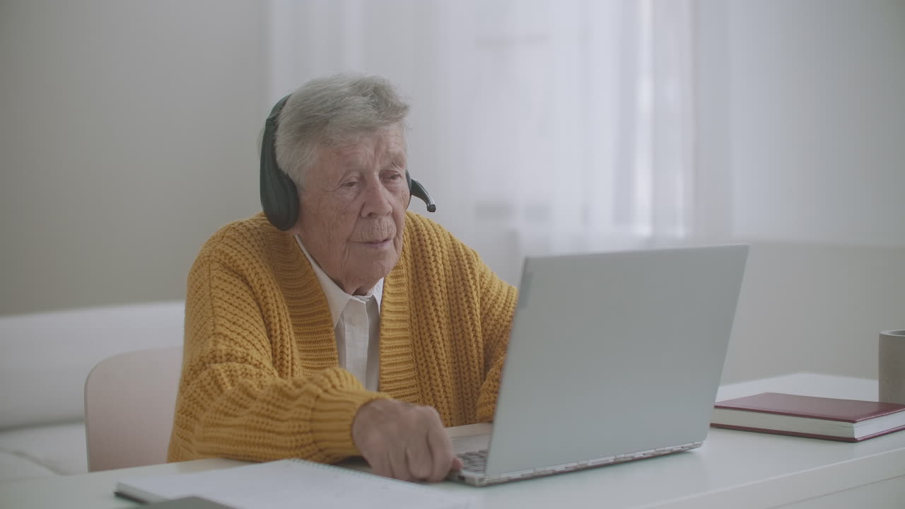 elderly Woman are using laptop to make video call talking gesturing showing thumbs-up hand gesture indoors. Old woman and modern devices concept.