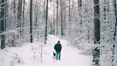 a man with a camouflage jacket walks along with a puppy dog on a snow train in the forest