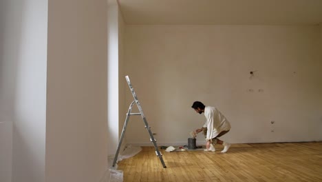 man on floor dipping paintbrush into bucket with limewash paint in house