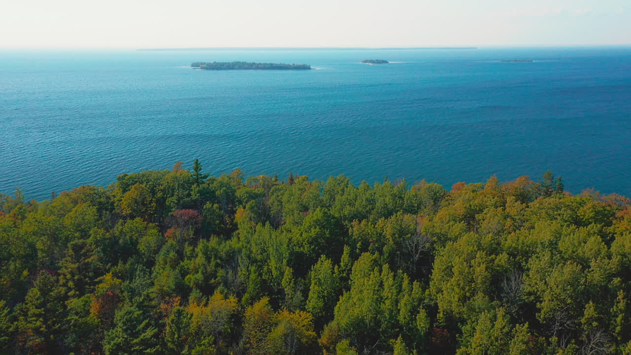 From above, the northern edge of Door County reveals a vast sweep of emerald forest and deep blue lake, with small islands scattered across the calm horizon under clear skies