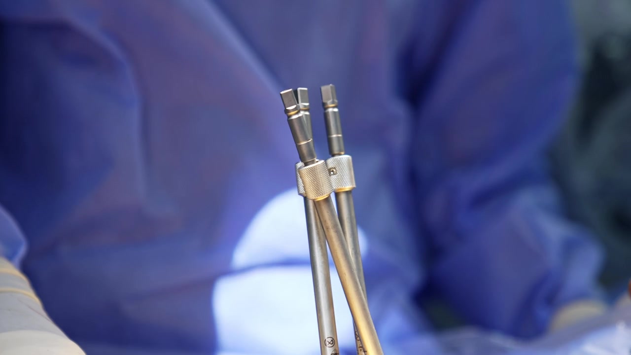 Tre strumenti chirurgici metallici uniti durante un'operazione neurochirurgica. Primo piano degli strumenti utilizzati in chirurgia. Un medico non riconoscibile lavora sullo sfondo.