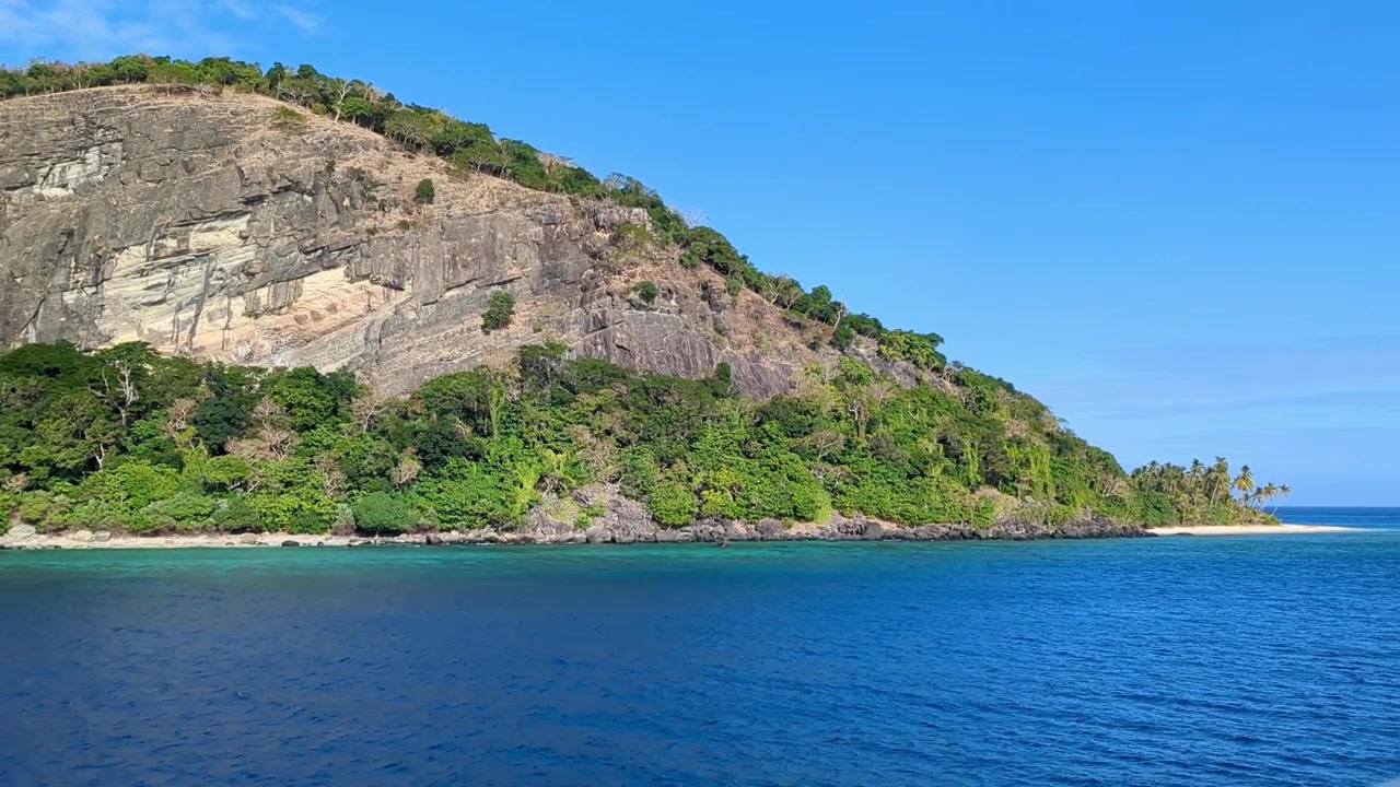 Navigando oltre un'isola tropicale remota e aspra con una parete rocciosa a picco e una spiaggia di sabbia bianca nelle Isole Yasawa, Fiji, Pacifico del Sud.