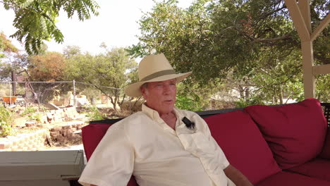 Handsome-older-caucasian-man-sits-relaxed-in-patio-chairs,-talking-to-someone