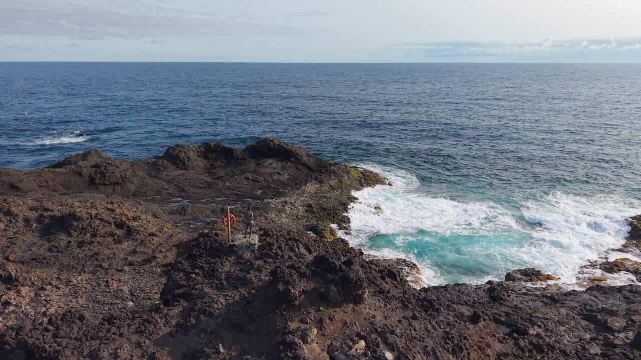 Woman standing on volcanic rocks near Punta Sardina lighthouse, Gran Canaria, admiring breathtaking ocean view