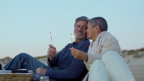 feliz pareja caucásica senior sosteniendo bengala y disfrutando el tiempo juntos en la playa