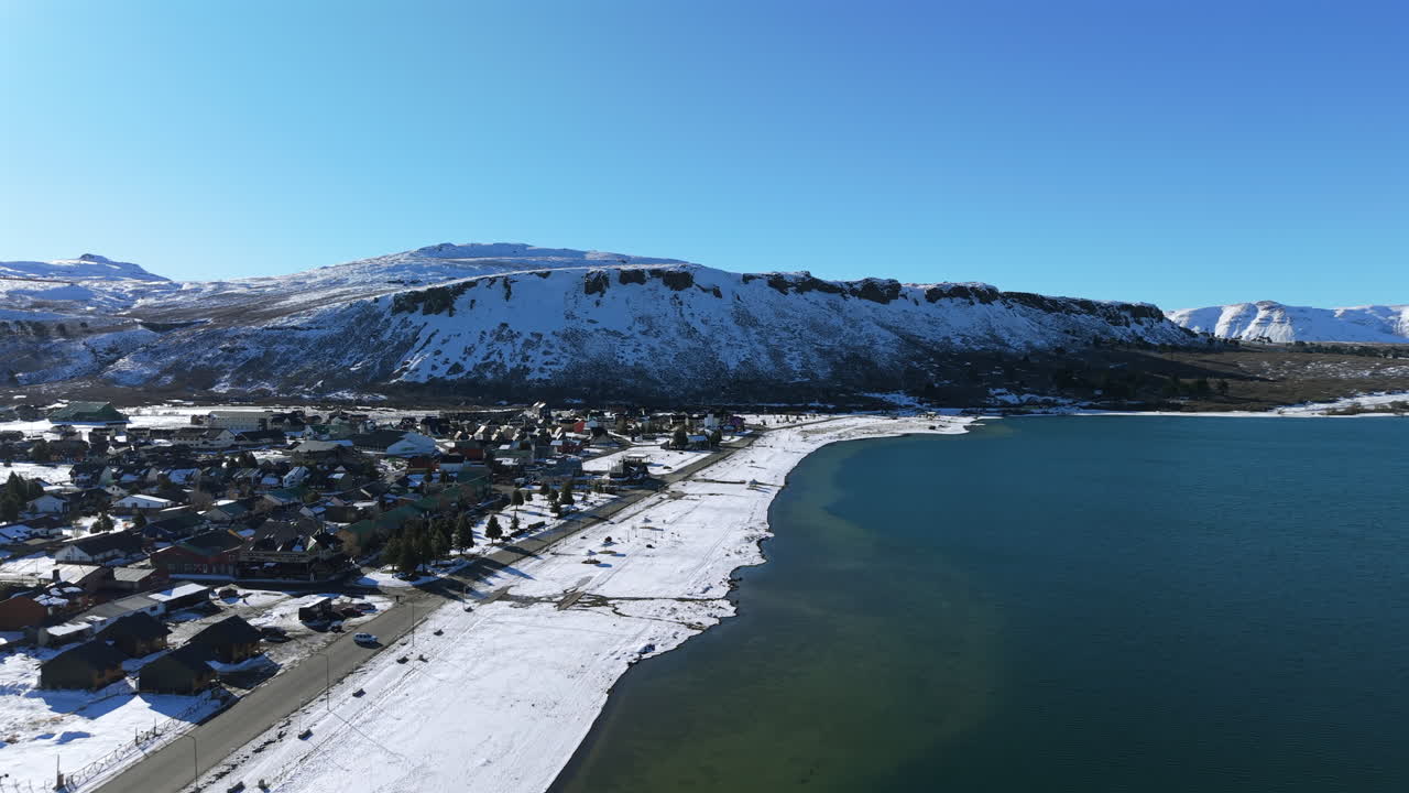 Aerial footage of Caviahue town in Neuquén, Argentina, showing the snowy shoreline of the lake with mountains in the background