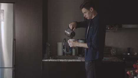 man pouring coffee in mug in the kitchen at home - medium shot