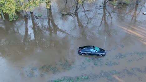 High-aerial-of-lonely-stranded-water-damaged-car-in-river-flood-water-after-hurricane,-storm-damage,-totaled-vehicle