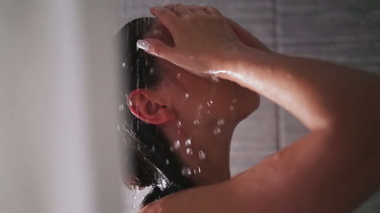 Woman and splashing water in shower cabin. Attractive lady relaxes washing hair and skin in hot water sprays at home. Woman at spa procedures