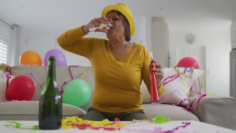 African-american-senior-woman-celebrating-with-champagne-and-party-blower,-on-new-year's-video-call