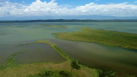 綠色和棕色海洋水域的草地島<unk>, 周圍是山脈, 無人機空中