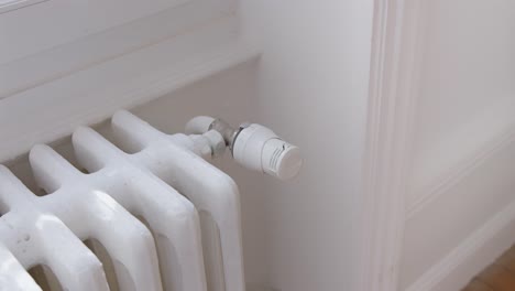 hand of woman adjust radiator temperature to reduce heating expenses, close up