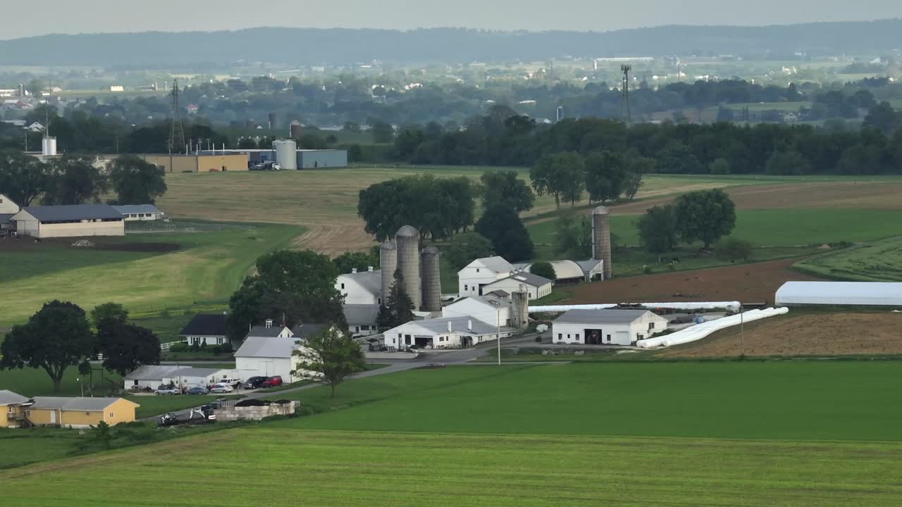Aerial wide shot of silo storage on farmers house of american city. Green cropland fields and american neighborhood in Pennsylvania. Cloudy and foggy day at dusk in summer.