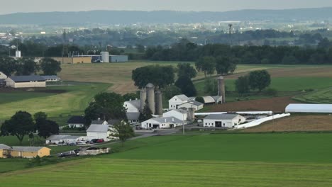 aerial wide shot of silo storage on farmers house of american city. green cropland fields and american neighborhood in pennsylvania. cloudy and foggy day at dusk in summer.