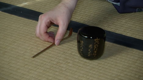 una cuchara de té de bambú y un bote de té descansan sobre una estera de tatami durante una ceremonia japonesa del té