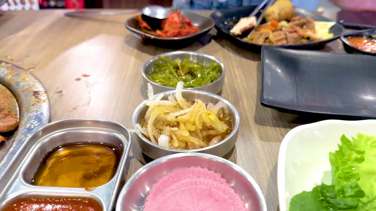 Korean BBQ with vibrant dishes and grilling meats in a lively Bangkok setting. Bright lighting enhances the colorful, appetizing presentation