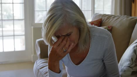 front view of mature caucasian woman crying while sitting on the couch in living room at home 4k