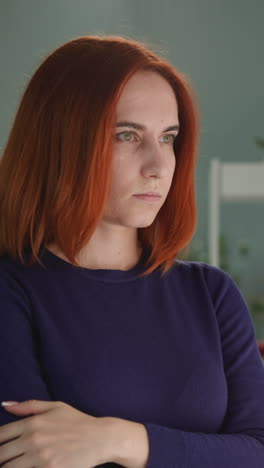 depressed woman with ginger hair looks out bright window with white curtains. housewife feels sad standing in bedroom with crossed arms closeup