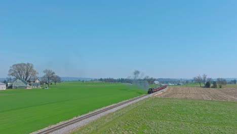 a drone stationary view of a steam passenger train approaching thru farmlands, blowing smoke on a spring day
