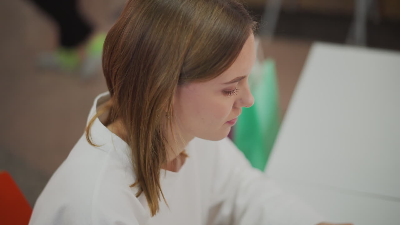 взгляд сверху на молодую женщину, сосредоточенную на работе, демонстрирующую современный образ жизни и производительность в яркой внутренней среде с красочными сумками для покупок на заднем плане