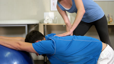 fisioterapeuta femenina ayudando a un hombre con una pelota de ejercicio