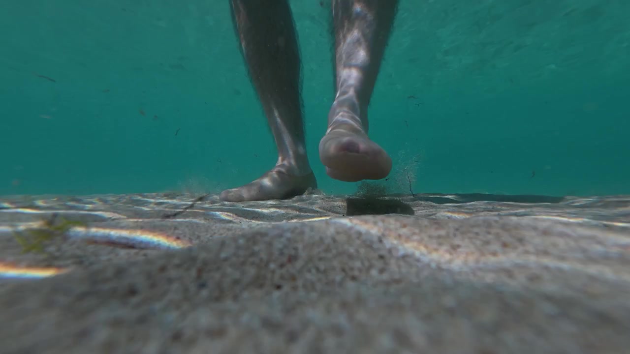 Vista subacquea di una persona che cammina a piedi nudi sul fondale marino. Concetto di consapevolezza della sicurezza che evidenzia i potenziali rischi da rocce affilate, conchiglie, ricci di mare e superfici subacquee irregolari.