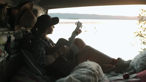 Mujer-Sentada-En-Una-Furgoneta-Con-Perro-Y-Tocando-La-Guitarra