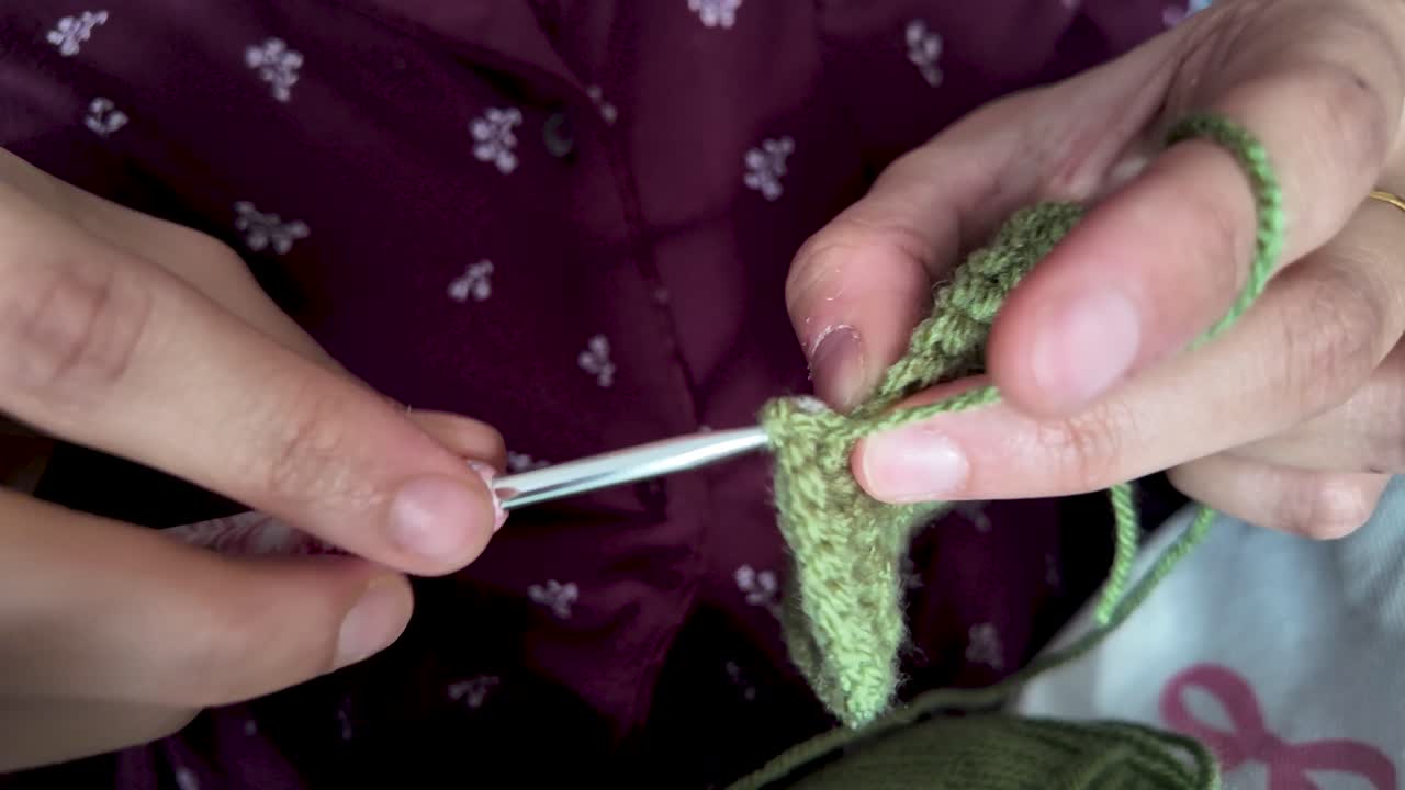 Primo piano di mani che lavorano all'uncinetto filato verde con un uncinetto d'argento per artigianato e hobby, mostrando il processo di cucitura e la creazione tessile.