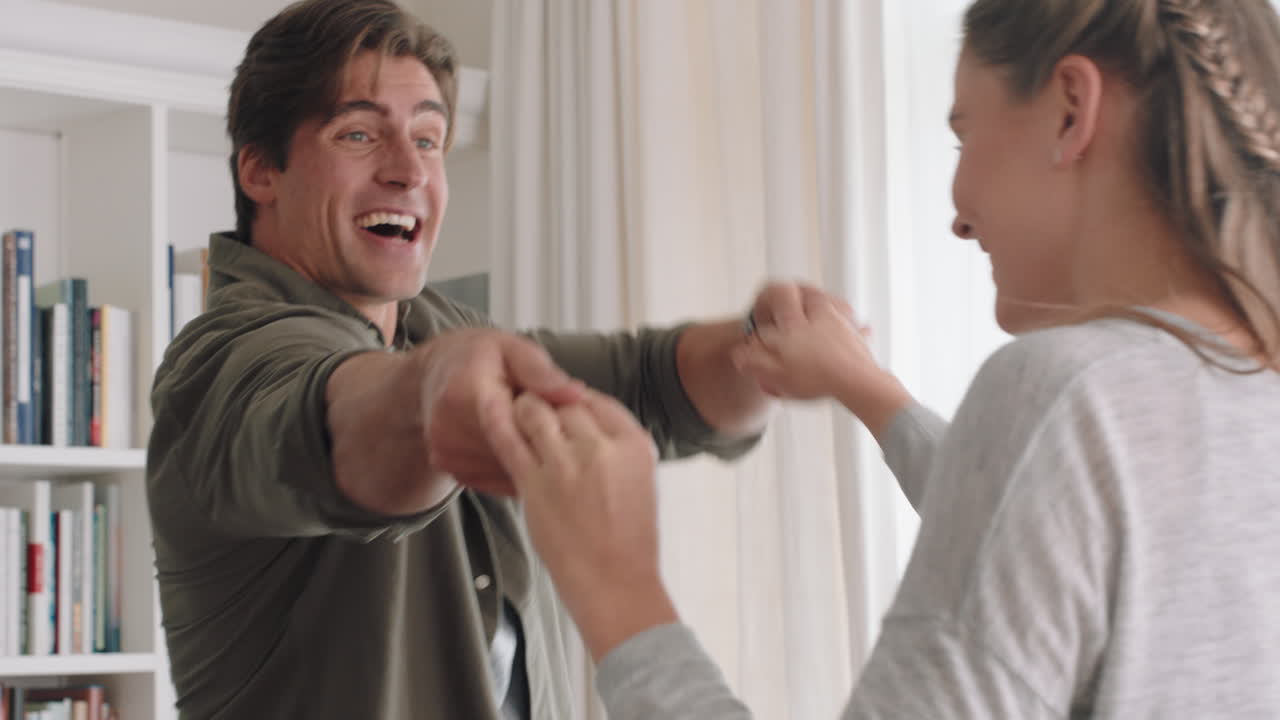 행복한 젊은 커플이 집에서 함께 춤을 추고 축하하고 즐거운 주말을 보내며 웃으며 거실에서 재미있는 춤을 즐기고 성공적인 관계 축하 4k 영상