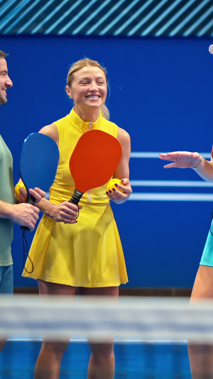 Two men and two women high-fiving after playing pickleball on a blue, inside court. Vertical