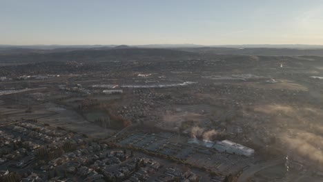 wide angle drone birdseye footage over city in central valley in california, usa on a sunny misty morning, with mountains in the distance