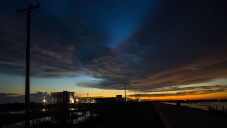 Power-energy-cable-posts-silhouetted-alongside-road-with-traffic-with-vivid-sunset