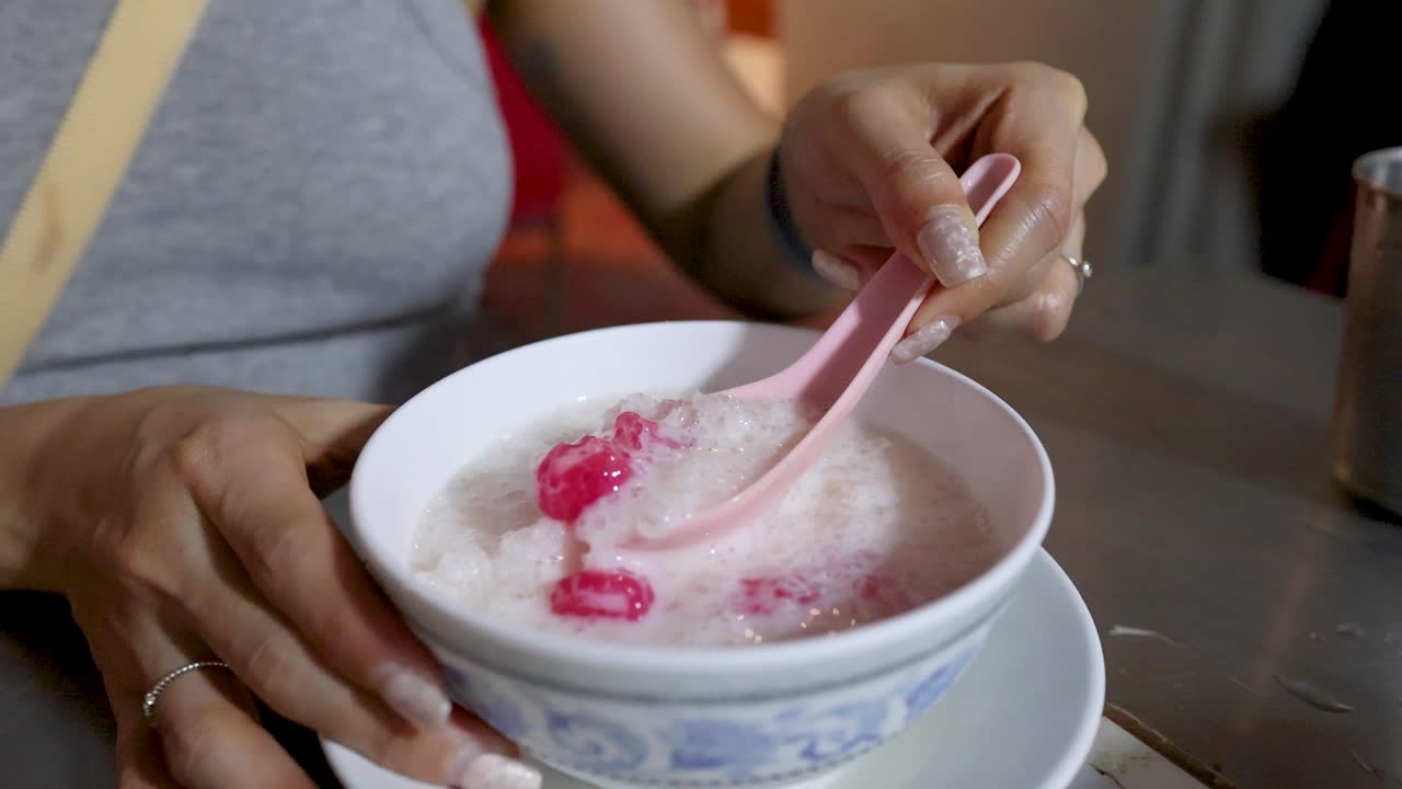 Close-up of woman stirring and scooping Thai red rubies dessert in outdoor street food setting