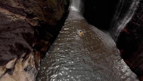 mesmerizing view of a tourist enjoying in the pond formed by isolated and uninhabited waterfall, amidst the steep brown rocky mountains