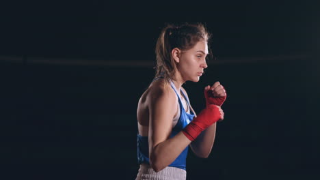 A-beautiful-woman-conducts-a-shadow-fight-practicing-technique-and-speed-of-strikes-while-training-hard-for-future-victories.-Dark-gym-background.-steadicam-shot