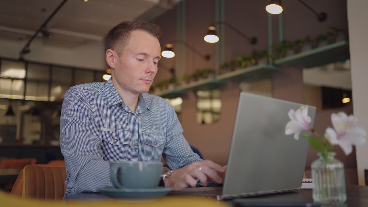 A serious man is a business student working studying sitting at a table and typing a message on a laptop. Typing text on the keyboard
