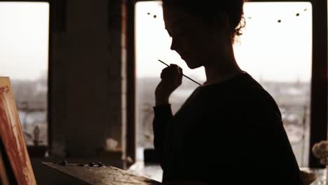 expressive female artist. talanted young girl taking paint palette off the table and then adding some paint expressively to her picture.