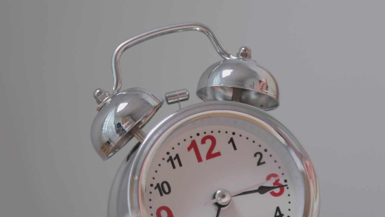 아침에 테이블 위에 있는 옛날의 알람 시계가 울리자, 소녀의 손은 알람을 뒤집어 닫고, 잠자는 소녀는 알람을 울리면서 깨어나서 알람을 꺼낸다.