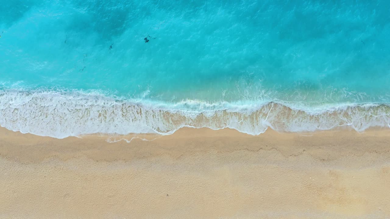 Serene aerial view of Myrtos Beach, Kefalonia, showing pristine azure waters and white pebble shores surrounded by lush greenery under a brilliant sunny sky.