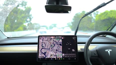 tesla interior with autopilot navigation during a rainy drive on gold coast. clear screen display, windshield wipers active