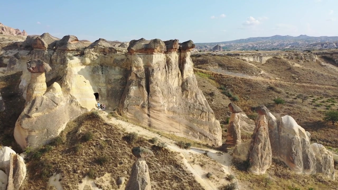 Berrak mavi bir gökyüzünün altında, Güllüdere Vadisi, Kapadokya, Nevşehir, Türkiye'deki beyaz kaya oluşumlarının, konik peri bacalarının ve düz tepeli tüf dağlarının panoramik havadan drone görüntüsü.