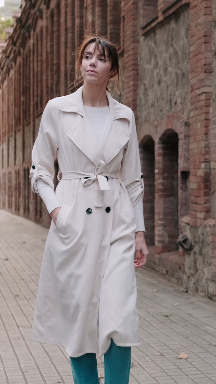 Giovane Donna in Trench che Cammina per una Vecchia Strada di Città.