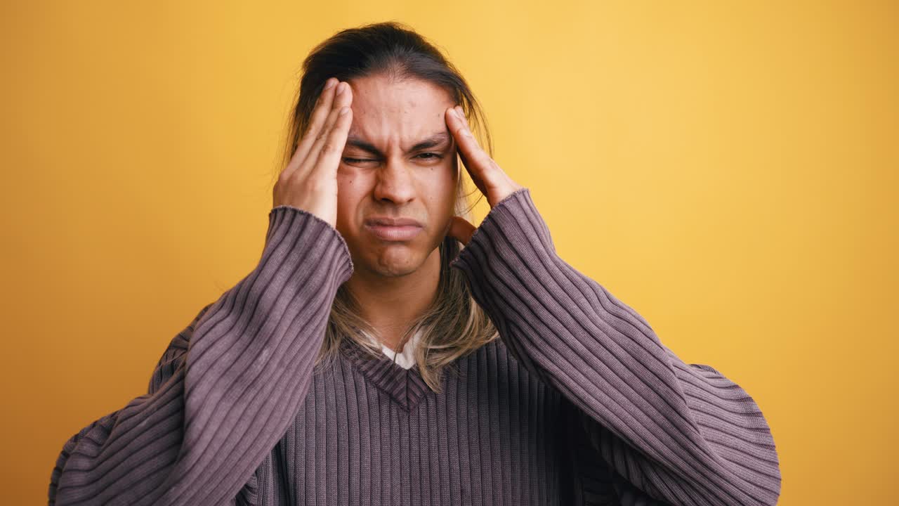 Young Man Suffering from Headache or Stress on Yellow Background