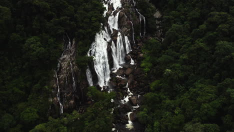 Drone-shot-tilting-toward-a-steep-waterfall,-cloudy-day-in-Barro-da-Sahy,-Brazil