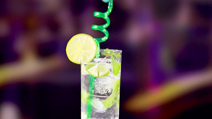 Un vivace cocktail mojito con lime e una cannuccia a spirale in un ambiente vivace e colorato. L'illuminazione brillante esalta l'atmosfera rinfrescante.