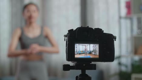 close up de un monitor de cámara grabando entrenadora asiática mujer en ropa deportiva hablando y haciendo cardio rodillas altas mientras enseña ejercicios en casa