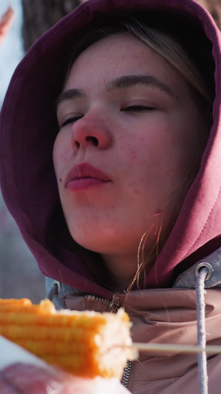 mulher comendo milho em um parque ao ar livre com folhas secas balançando suavemente acima, desfrutando de um lanche no inverno, reflexo de luz suave no fundo, atmosfera tranquila do parque, cena de inverno com uma brisa leve