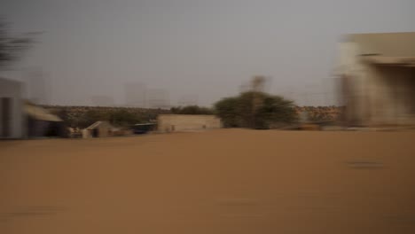 a shot of the senegal landscape taked from a car, showing some houses, trees, and a lot of sand