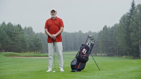 older man standing on golf course with golf clubs